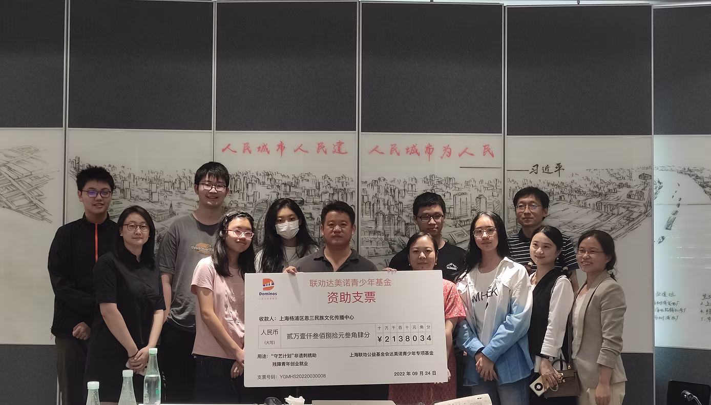 The ten-person Domino Youth Philanthropy team posing with a large ceremonial donation check for Ensan National Culture Dissemination Center