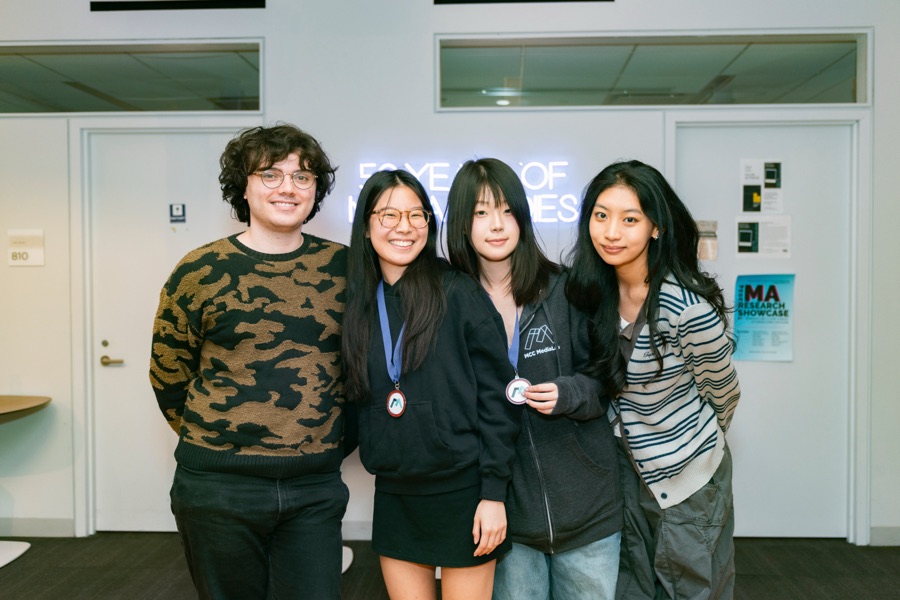 Core design team smiling together in front of a neon MediaLab sign