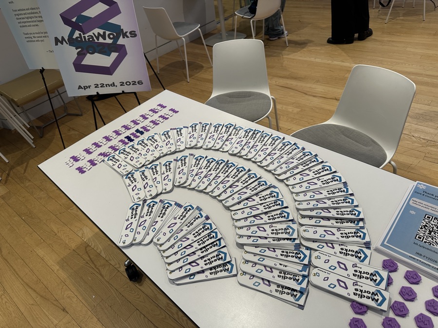 Welcome table at the MediaWorks 2026 event, fanned out with printed programs and buttons