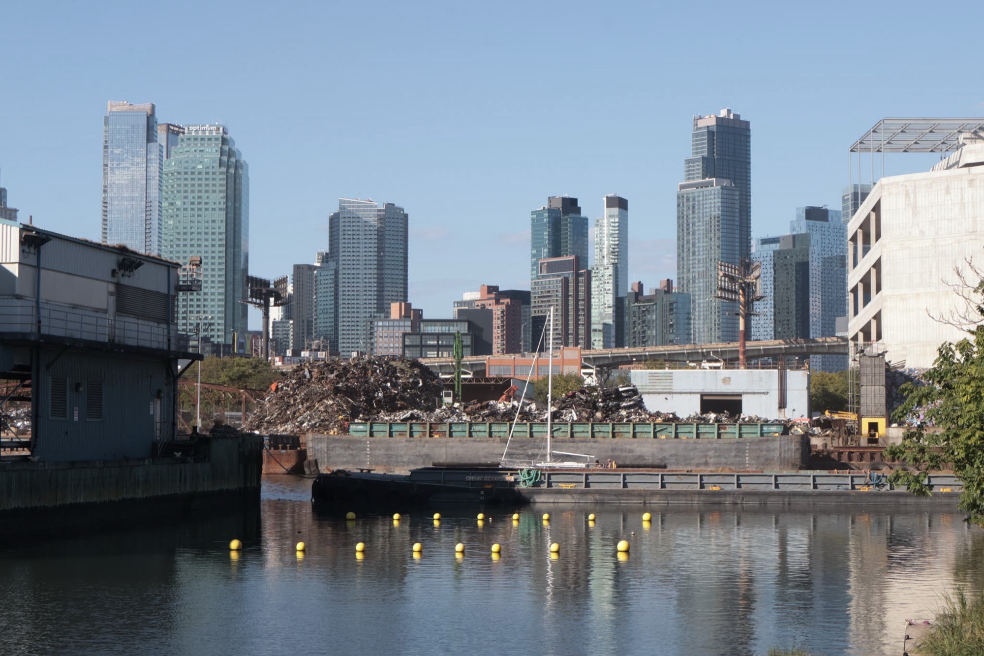 The Manhattan skyline reflected across Newtown Creek, with industrial debris in the foreground