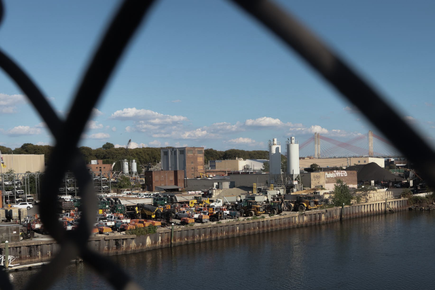 Newtown Creek's industrial shoreline viewed through a chain-link fence