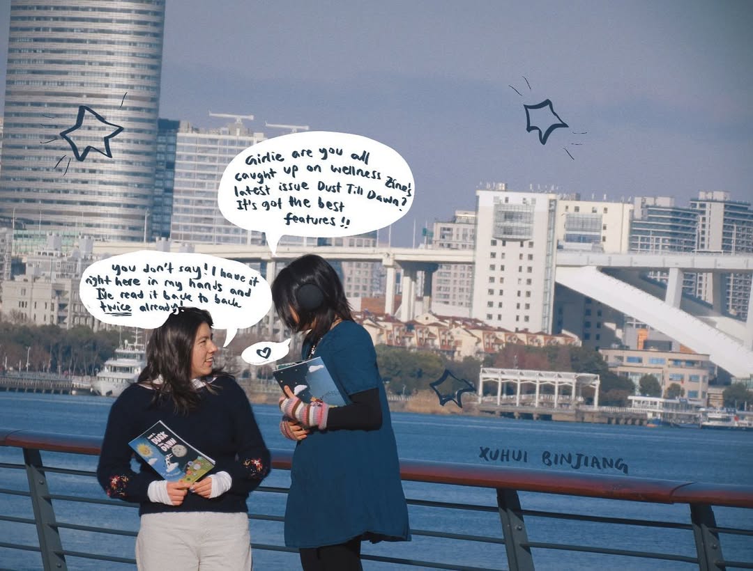 Two people talking on a riverfront railing holding the printed zine, with comic-style speech bubbles about the latest issue drawn over the photo